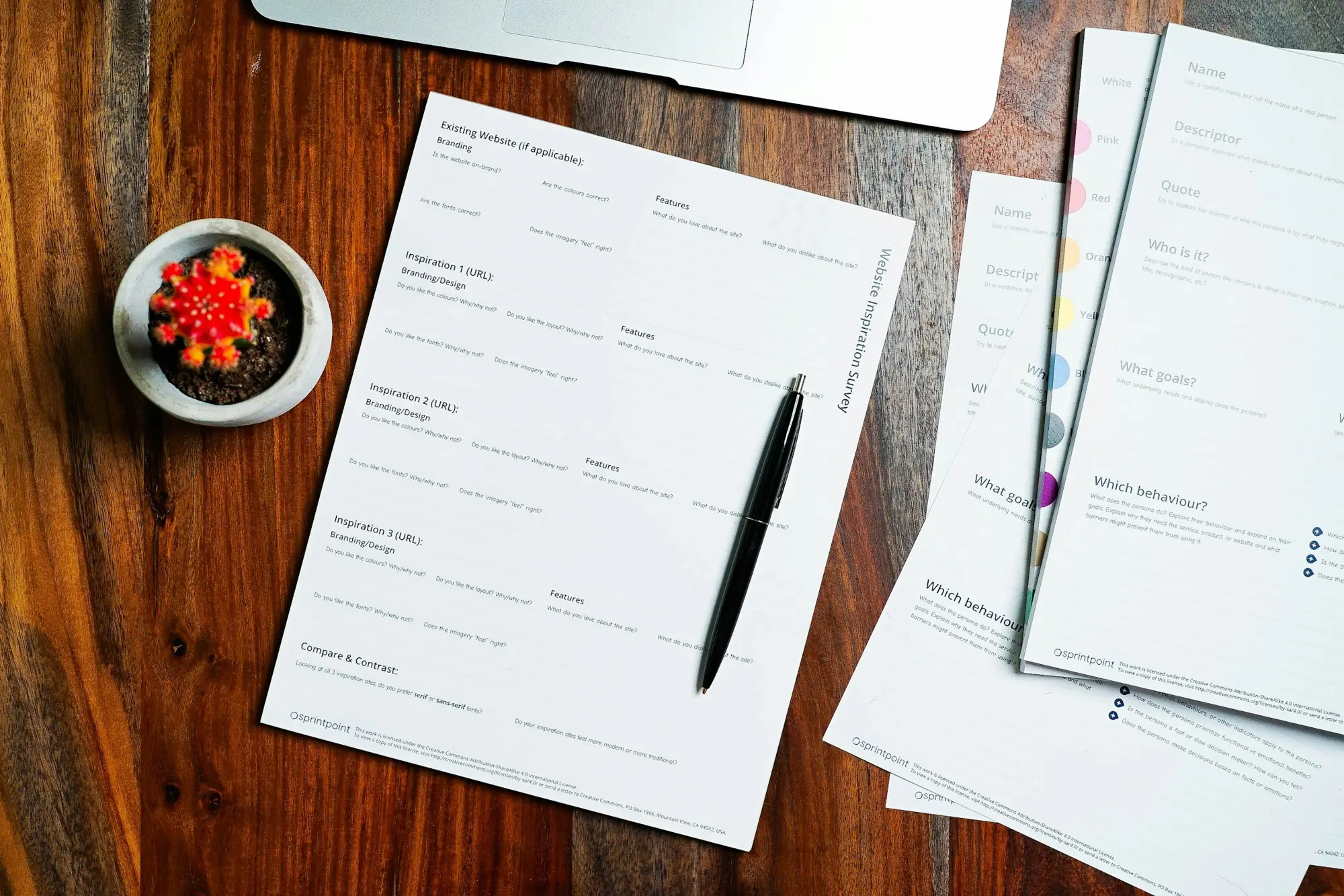 Documents laid out on a walnut desk beside a pen